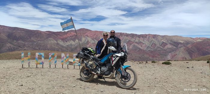 Dos riders y su moto frente al Cerro de los Siete Colores, en Purmamarca
