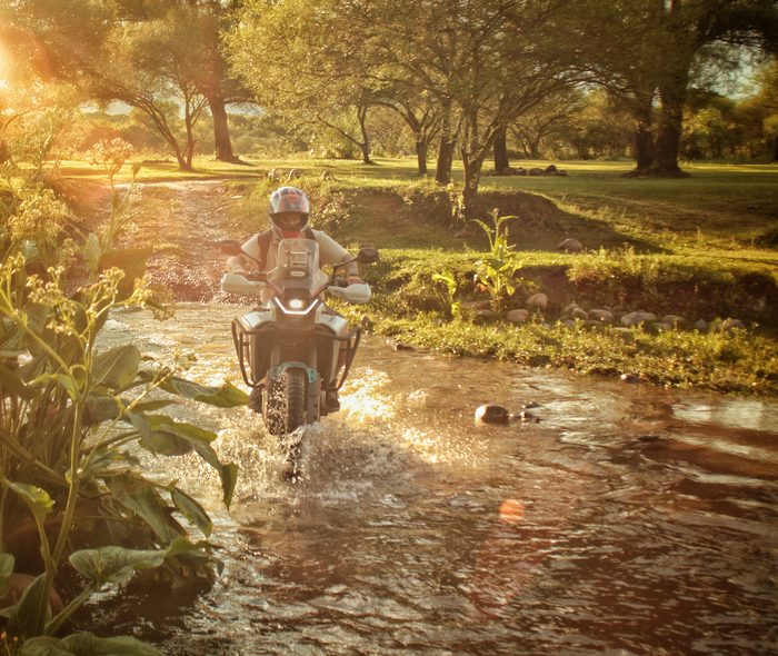Moto cruzando un río poco profundo entre la arboleda